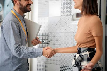 Tile stores near me—professionals shaking hands in creative showroom with design patterns on glass wall.